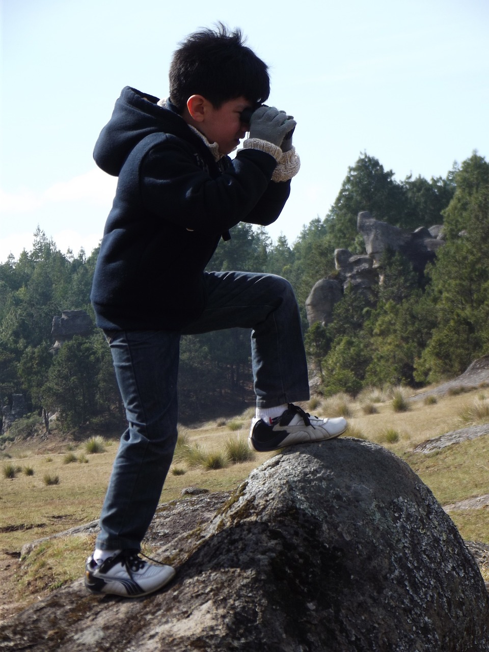 Boy standing on rock looking through binoculars